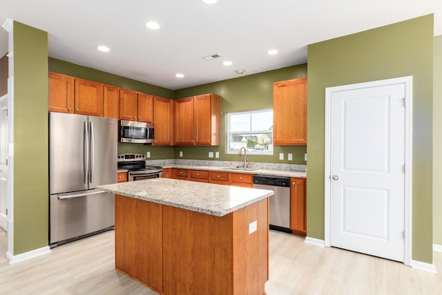 kitchen with sink, appliances with stainless steel finishes, a center island, light stone counters, and light wood-type flooring