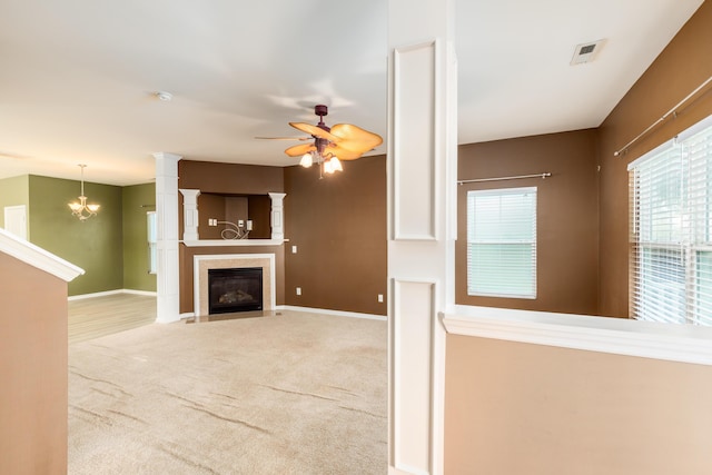 unfurnished living room featuring decorative columns, ceiling fan with notable chandelier, and light carpet