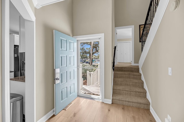 foyer entrance featuring stairs, light wood-type flooring, and baseboards