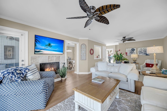 living room with ornamental molding, a tile fireplace, light wood-style floors, and ceiling fan