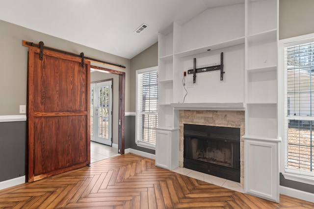 unfurnished living room with lofted ceiling, visible vents, a tiled fireplace, a barn door, and baseboards