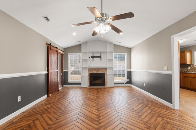 unfurnished living room featuring lofted ceiling, a barn door, a fireplace, visible vents, and a ceiling fan