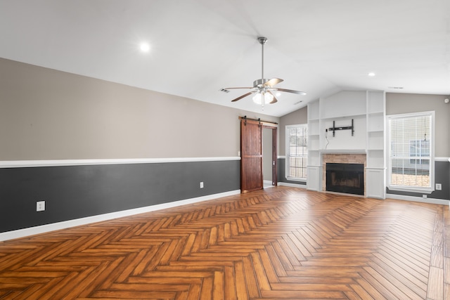 unfurnished living room featuring lofted ceiling, a barn door, a fireplace, a ceiling fan, and baseboards