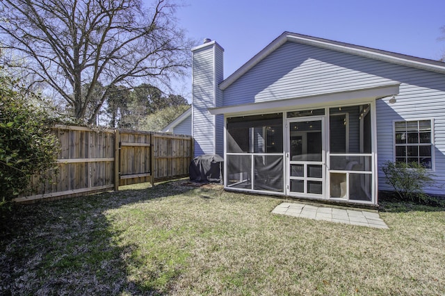 back of house featuring a lawn, a chimney, a sunroom, and fence