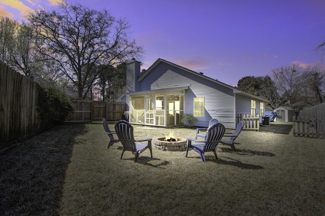 back of house at dusk with a chimney, a fire pit, a fenced backyard, and a sunroom