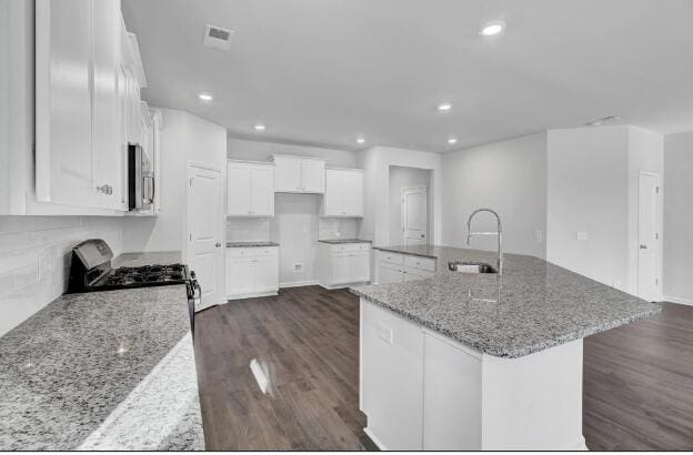 kitchen with sink, a large island with sink, stainless steel appliances, white cabinets, and light stone countertops