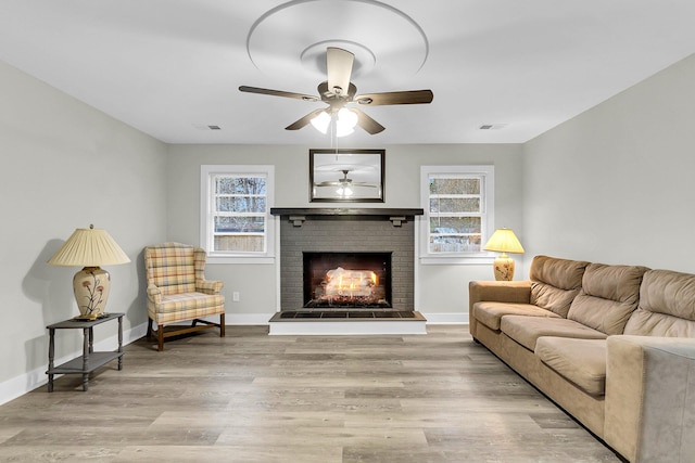 living room featuring light hardwood / wood-style floors, a brick fireplace, ceiling fan, and a healthy amount of sunlight