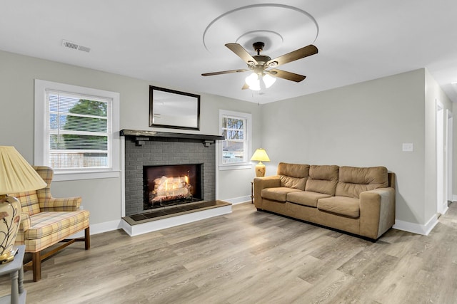 living room with ceiling fan, light hardwood / wood-style floors, and a brick fireplace