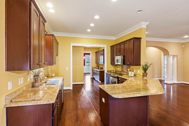 kitchen with kitchen peninsula, dark hardwood / wood-style floors, stainless steel appliances, and decorative columns