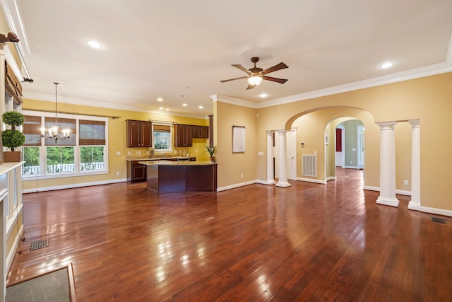 unfurnished living room with ceiling fan with notable chandelier, decorative columns, dark wood-type flooring, and crown molding