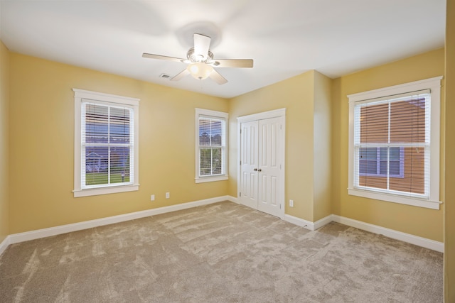 unfurnished bedroom featuring multiple windows, light colored carpet, ceiling fan, and a closet