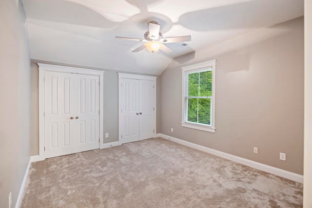 unfurnished bedroom featuring multiple closets, vaulted ceiling, light colored carpet, and ceiling fan