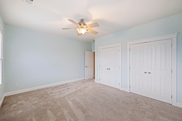 unfurnished bedroom with carpet, ceiling fan, and two closets