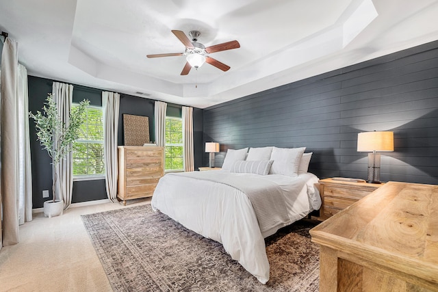 bedroom with a ceiling fan, visible vents, wood walls, carpet, and a tray ceiling