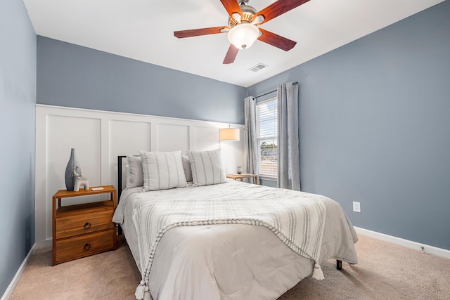 bedroom featuring ceiling fan, visible vents, light carpet, and a wainscoted wall