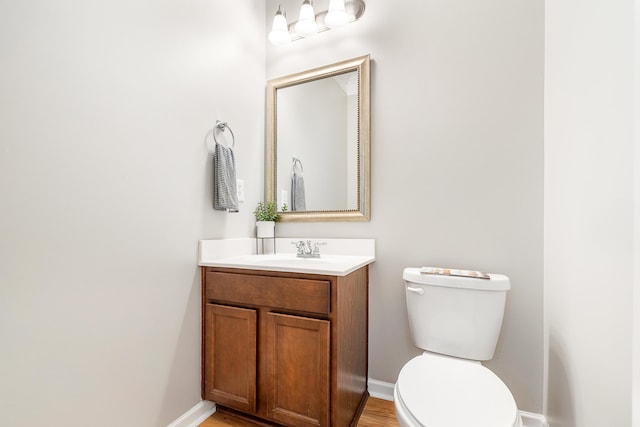 half bathroom with vanity, baseboards, and toilet