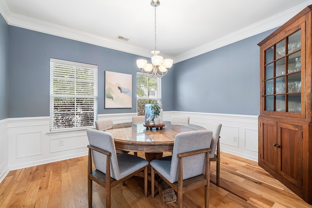 dining space with a wainscoted wall, ornamental molding, light wood finished floors, and a chandelier