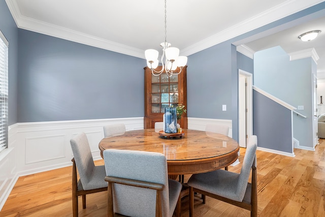 dining room featuring crown molding, a wainscoted wall, a notable chandelier, and light wood-type flooring