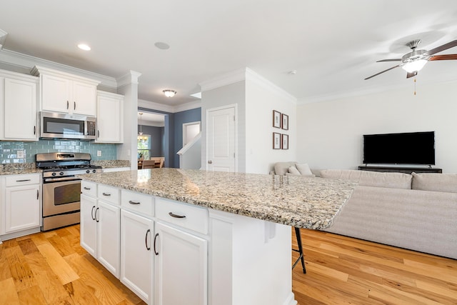 kitchen featuring crown molding, light wood-style flooring, stainless steel appliances, open floor plan, and a ceiling fan