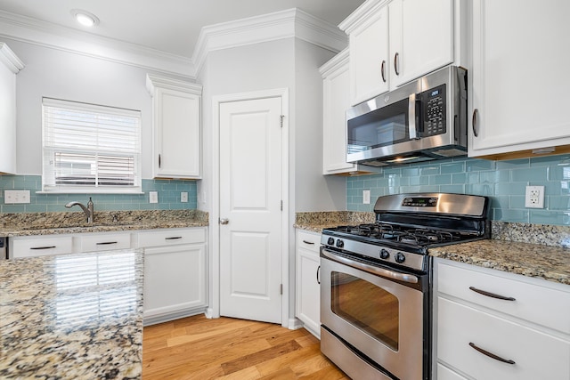 kitchen with ornamental molding, white cabinetry, a sink, light wood finished floors, and appliances with stainless steel finishes