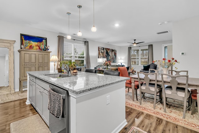 kitchen featuring sink, dishwasher, hanging light fixtures, light stone countertops, and an island with sink