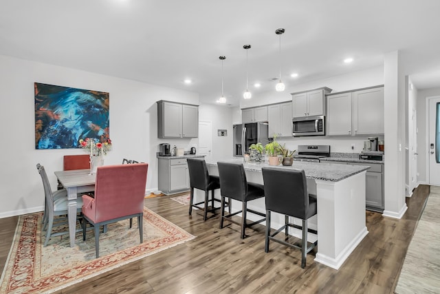 kitchen featuring pendant lighting, stainless steel appliances, a kitchen island with sink, and gray cabinetry