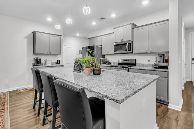 kitchen with appliances with stainless steel finishes, gray cabinets, hanging light fixtures, and a center island with sink