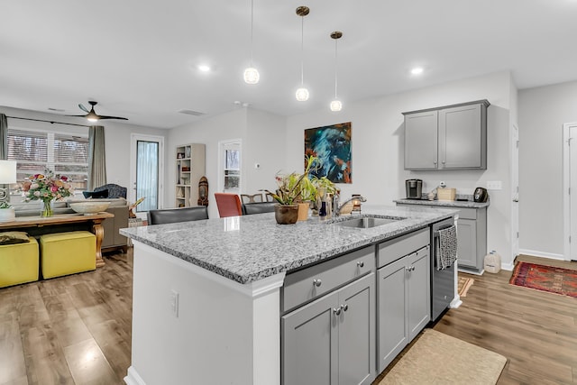 kitchen featuring light hardwood / wood-style flooring, gray cabinets, light stone countertops, an island with sink, and decorative light fixtures