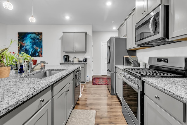 kitchen featuring gray cabinets, appliances with stainless steel finishes, pendant lighting, sink, and light stone counters