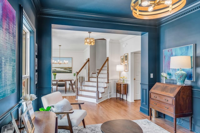 sitting room with ornamental molding, wainscoting, wood finished floors, stairway, and a chandelier