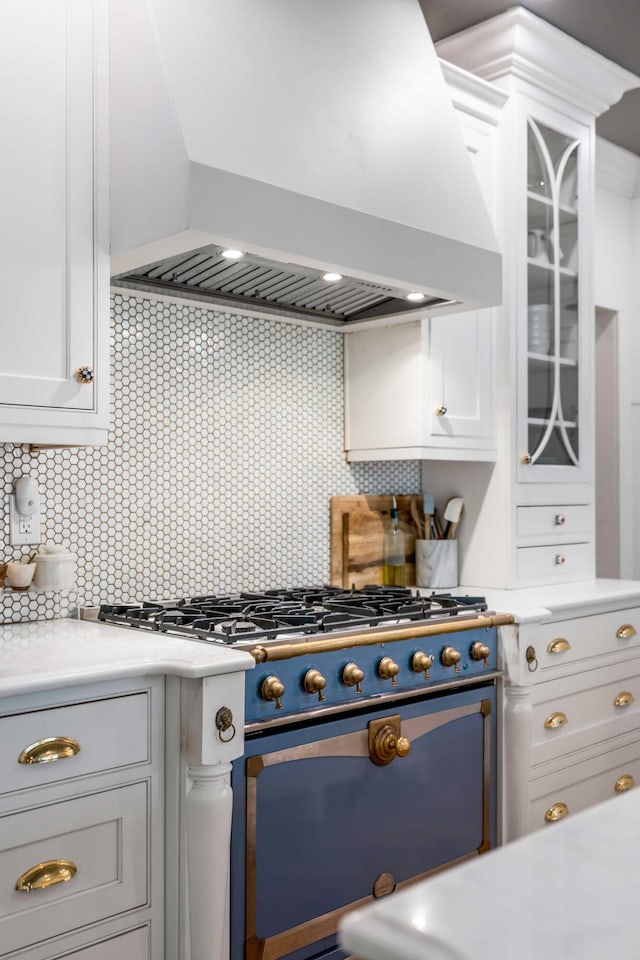 kitchen featuring light countertops, premium range hood, white cabinetry, glass insert cabinets, and range with gas cooktop