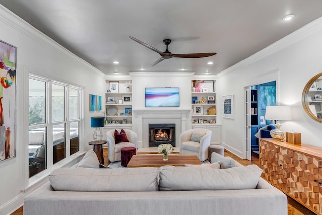 living room featuring baseboards, ceiling fan, a warm lit fireplace, and wood finished floors