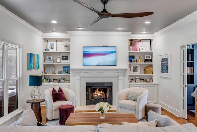 living room featuring crown molding, a ceiling fan, wood finished floors, and a warm lit fireplace