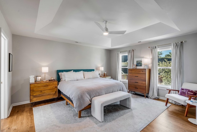 bedroom featuring ceiling fan, a raised ceiling, light wood-style flooring, baseboards, and visible vents
