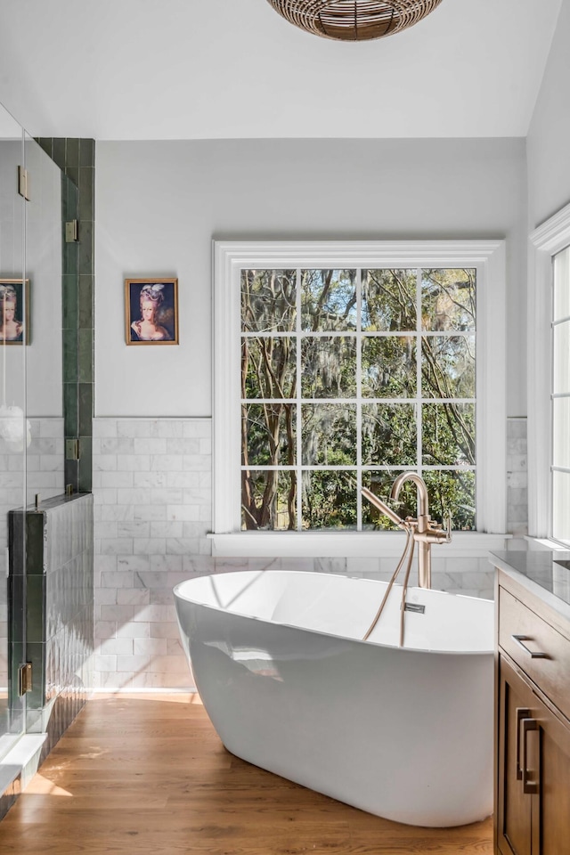 full bath with wood finished floors, a stall shower, a soaking tub, and tile walls