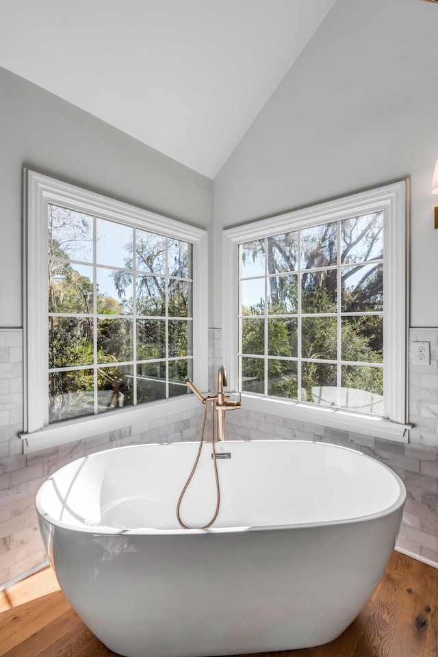 bathroom with a freestanding bath, tile walls, vaulted ceiling, and wood finished floors