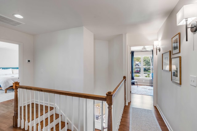 hall featuring baseboards, an upstairs landing, wood finished floors, and visible vents