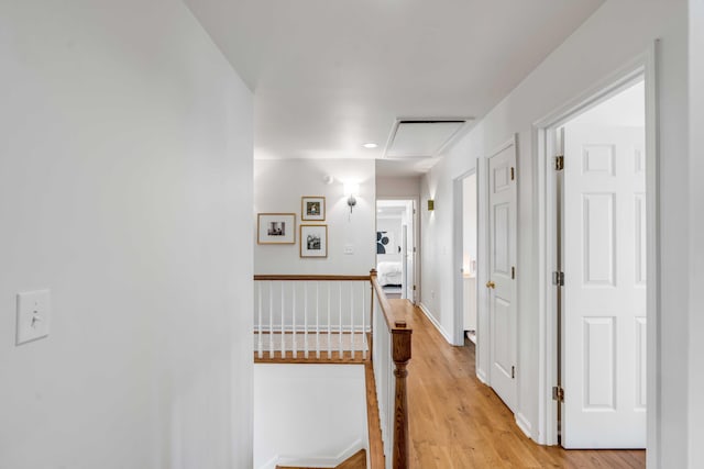 hall with baseboards, attic access, light wood finished floors, and an upstairs landing