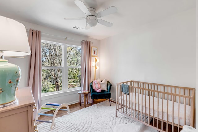 bedroom featuring baseboards, a crib, ceiling fan, and wood finished floors