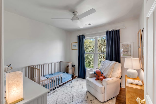 bedroom with ceiling fan, a crib, baseboards, wood finished floors, and visible vents