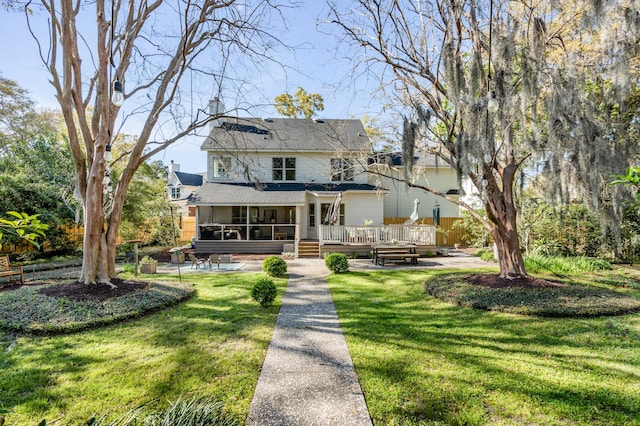 view of front of property with a sunroom, a front lawn, roof with shingles, and a wooden deck