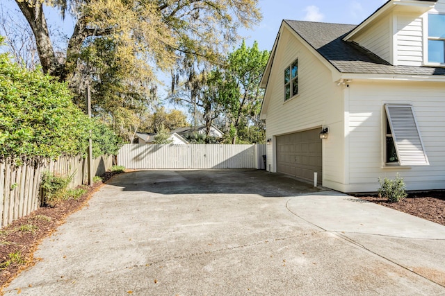 view of side of property featuring roof with shingles, a gate, fence, concrete driveway, and an attached garage