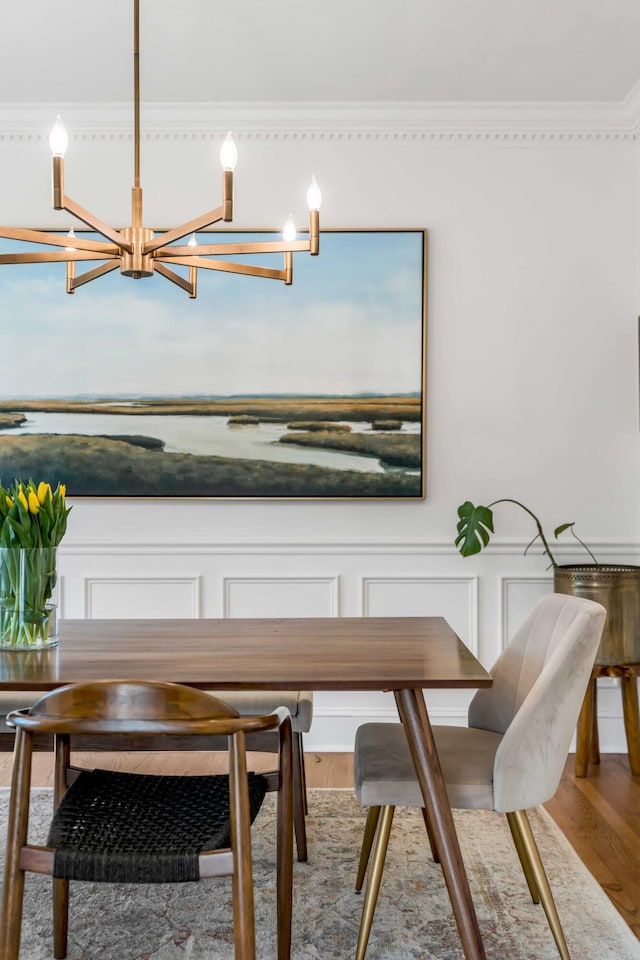 dining room with crown molding, an inviting chandelier, wood finished floors, and a decorative wall