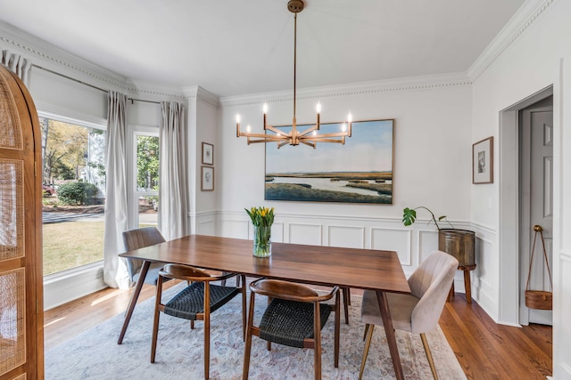 dining room with ornamental molding, wainscoting, wood finished floors, and a notable chandelier