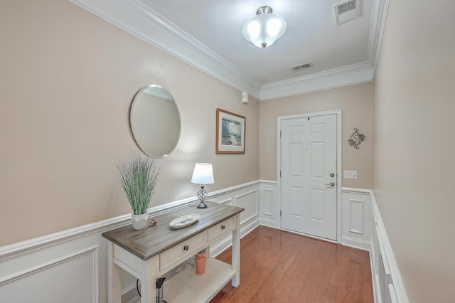 foyer entrance with a wainscoted wall, wood finished floors, visible vents, and crown molding