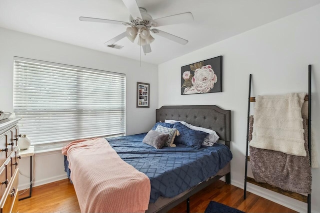 bedroom featuring a ceiling fan, wood finished floors, visible vents, and baseboards