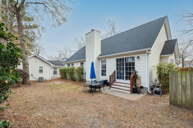 rear view of property with fence, entry steps, roof with shingles, central AC unit, and a chimney