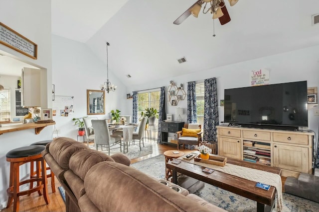 living room with visible vents, ceiling fan with notable chandelier, high vaulted ceiling, and light wood-type flooring