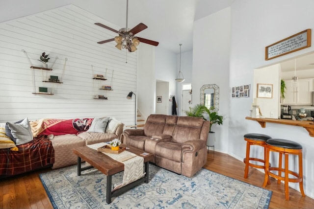 living room featuring stairway, a high ceiling, a ceiling fan, and wood finished floors