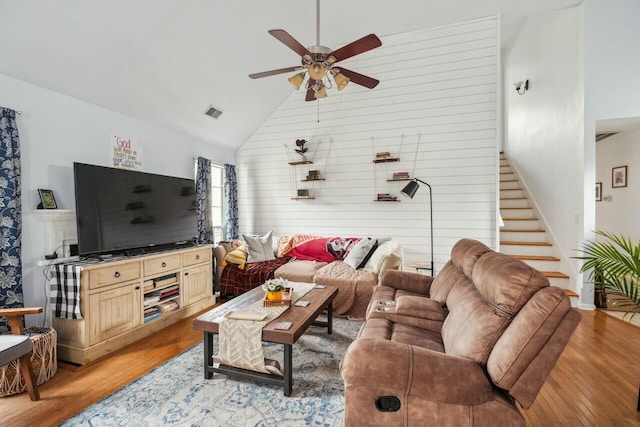 living area with a ceiling fan, visible vents, high vaulted ceiling, stairs, and light wood-style floors